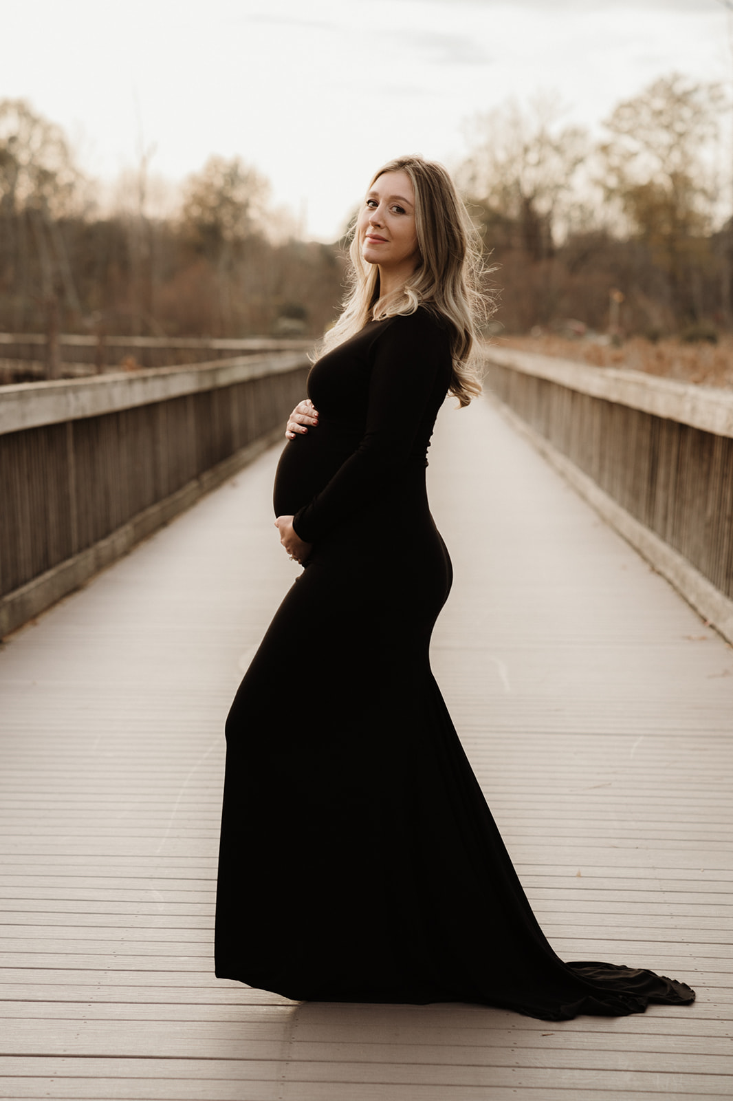 mom to be in black maternity gown cradling her bump on a boardwalk city of oaks Midwifery